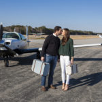 Young couple kissing as they walk away from private plane with luggage